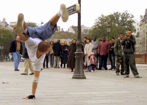 A breakdancer performing a one-handed freeze (also known as a pike) in the streets of Paris.